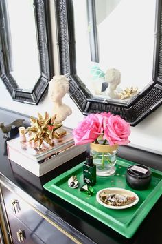 a green tray topped with pink flowers next to a mirror and other items on a table