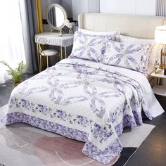 a white bed with purple flowers on it and a mirror in the corner behind it