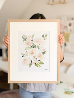 a woman holding up a painting with flowers on it