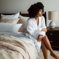 a woman sitting on top of a bed next to a night stand and nightstands