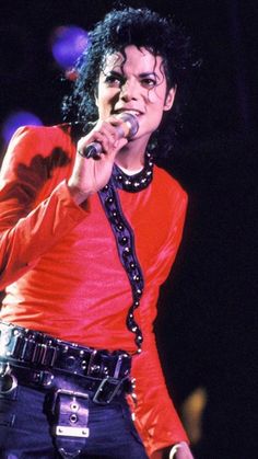 michael jackson performing on stage with his microphone in his hand and wearing an orange shirt