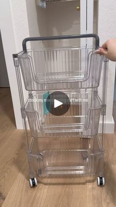 a person is pushing a clear plastic shopping cart with wheels on the floor in front of a white wall