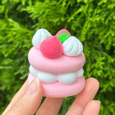 a hand holding a small pink cupcake with white frosting and a cherry on top