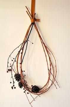 a piece of art made out of branches and pine cones hanging on a wall with a ribbon