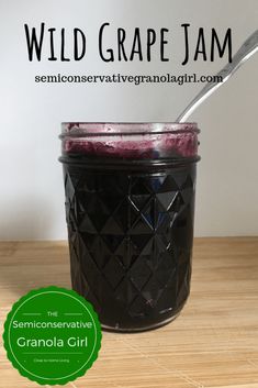 a glass jar filled with blueberry jam on top of a wooden table next to a spoon