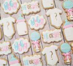 baby shower cookies are arranged on a wooden table with pink and blue decorations, including ones that say it's a boy or girl