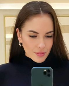 a woman looking at her cell phone while wearing earrings and a black top