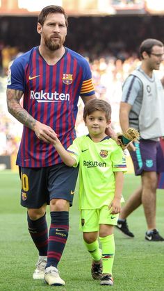 a man walking next to a little boy on top of a soccer field in front of a crowd