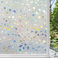 a window covered in lots of different colored glass shards next to a tree and bushes