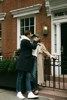 two people standing on the sidewalk in front of a brick building and one person taking a photo