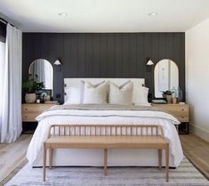 a bedroom with a large bed and two mirrors on the wall, along with a bench in front of it