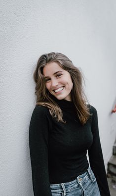 a smiling woman leaning against a white wall