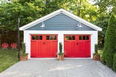 two red garage doors are on the side of a white and blue house with potted plants