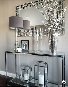 a glass console table with candles and flowers in front of a mirror on the wall