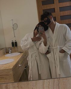 a man in a bathrobe taking a selfie with his cell phone while wearing a mask