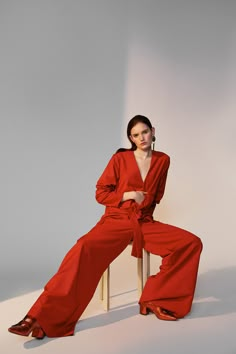 a woman sitting on top of a wooden chair wearing red pants and an orange shirt