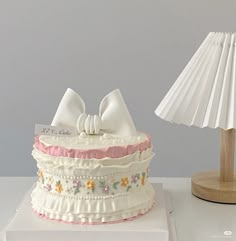 a white cake sitting on top of a table next to a lamp and paper shade