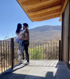 a man and woman standing on top of a balcony next to each other with mountains in the background