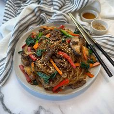 a white plate topped with meat and veggies next to two chopsticks