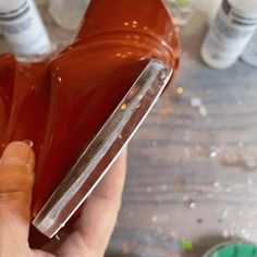 a person is holding a plastic container with some liquid on it and there are other bottles in the background