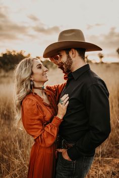 a man and woman standing together in the middle of an open field with tall grass