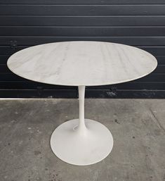 an oval marble table with white pedestals on concrete flooring in front of a garage door