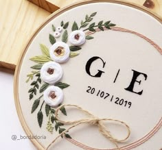 a close up of a embroidery on a wooden hoop with white flowers and green leaves