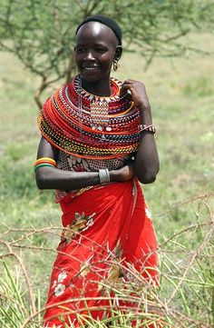 a woman in a red dress is standing by some bushes and trees with her arms wrapped around her neck