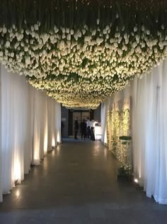 a long hallway with white curtains and flowers on the ceiling is lit up by lights