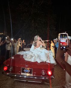 a bride and groom kissing in the back of a red convertible car with people taking pictures