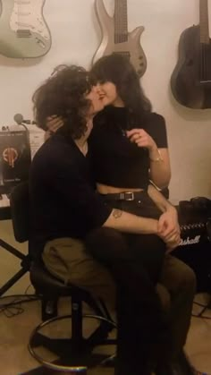 two people sitting in a room with guitars on the wall and one person kissing the other