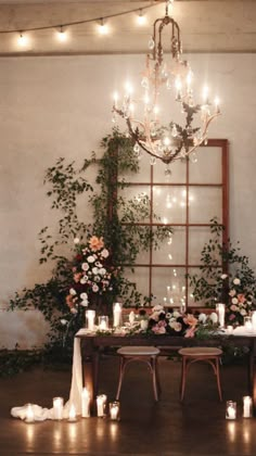 a table with candles and flowers on it in front of a chandelier filled with greenery