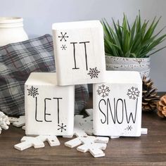 three wooden blocks with the words let it snow on them next to some pine cones