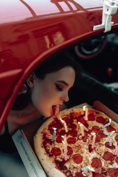 a woman blowing out candles on a pepperoni pizza in a box with the hood open