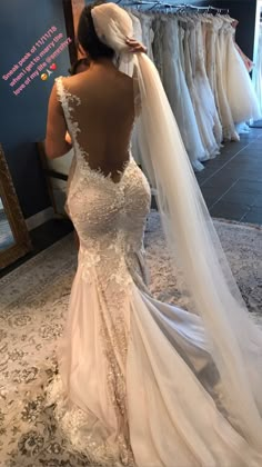 a woman in a wedding dress looking at the back of her gown, while she's wearing a veil