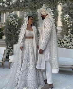 two people standing next to each other in front of a flower covered arch with white flowers