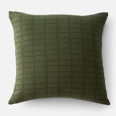 a green pillow with black squares on the front and back, sitting against a white wall