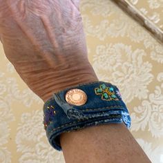 a person's arm with a blue jean bracelet and gold coin on the wrist