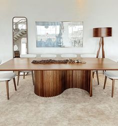 a large wooden table with white chairs and a mirror in the corner next to it