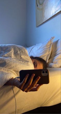 a woman is laying in bed and looking at her cell phone with the light on