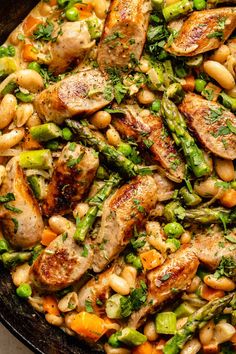 a skillet filled with chicken, beans and asparagus on top of a table