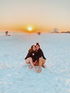 two women sitting on the beach at sunset with their arms around each other as they hug