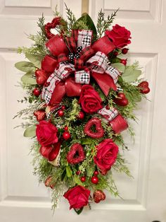 a wreath with red roses and greenery hanging on the front door for holiday decor