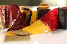 several pieces of fruit are arranged on a white plate with red and yellow strips next to them