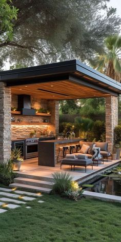 an outdoor kitchen and living room are shown in this backyard area with grass, trees, and water