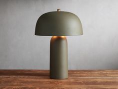 a green table lamp sitting on top of a wooden table next to a gray wall