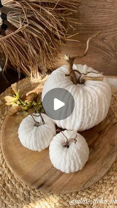 three white pumpkins sitting on top of a wooden board next to some dried leaves