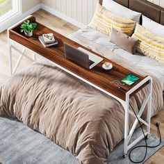 a bed with a laptop on top of it next to a table that has a plant in it