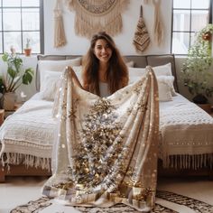 a woman sitting on top of a bed holding a christmas tree blanket over her face