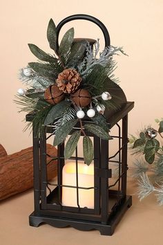 a candle is lit in front of a lantern with greenery and pine cones on it